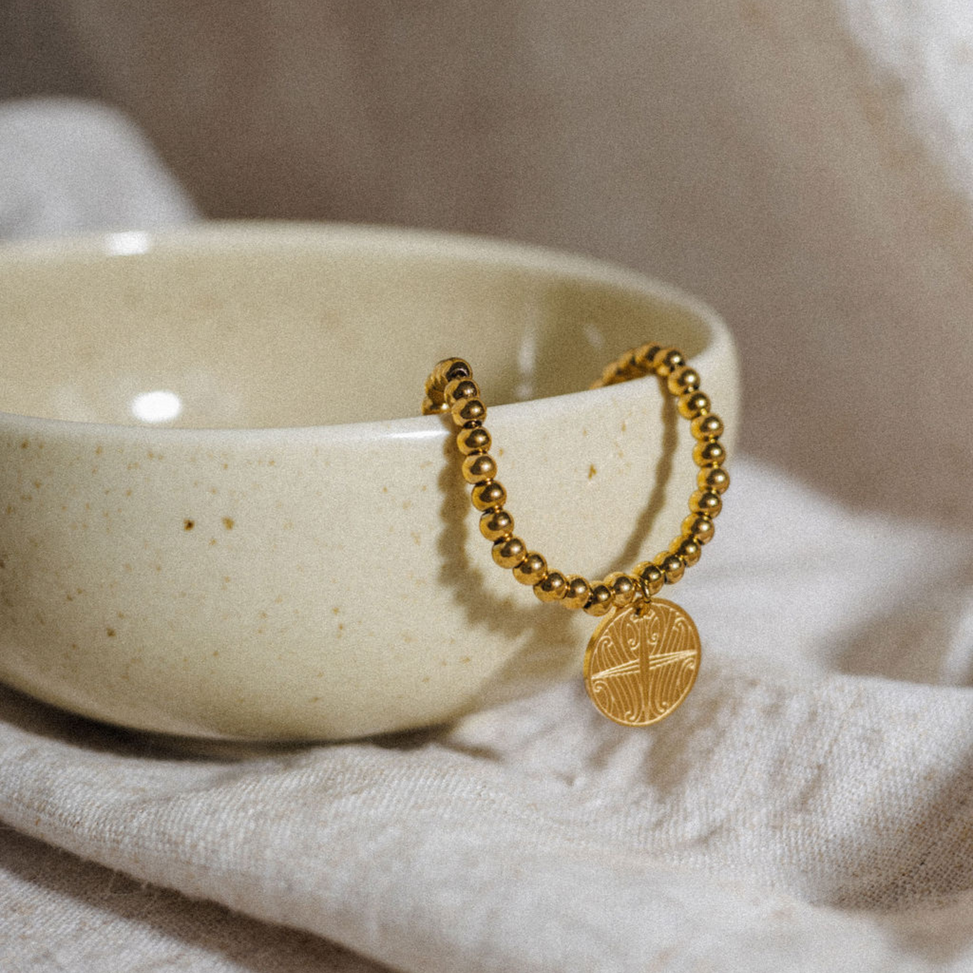 Gold plated Kāpehu Whetū Beaded Bracelet sitting in a clay jewellery bowl