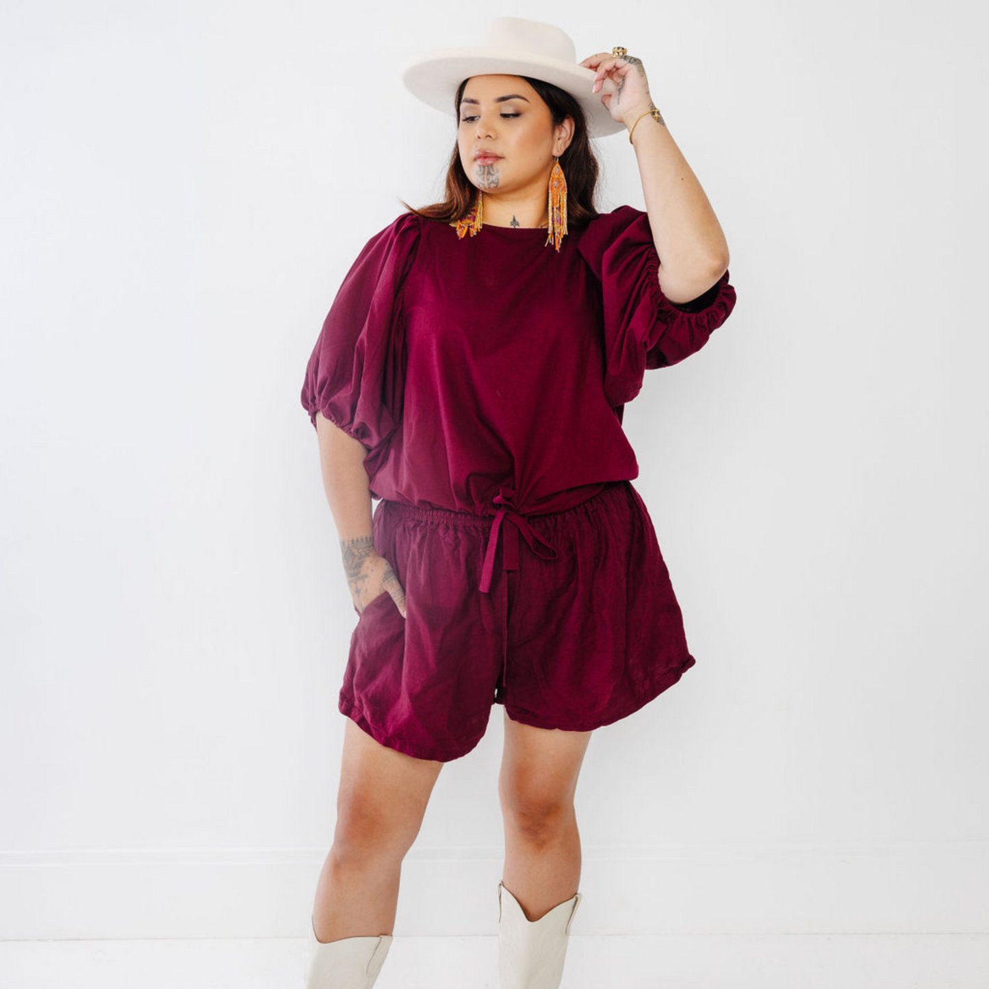 Jonique Oli, founder of Waiapu Road, wearing the Kapua Shorts - Plum - matched with a white hat and white boots