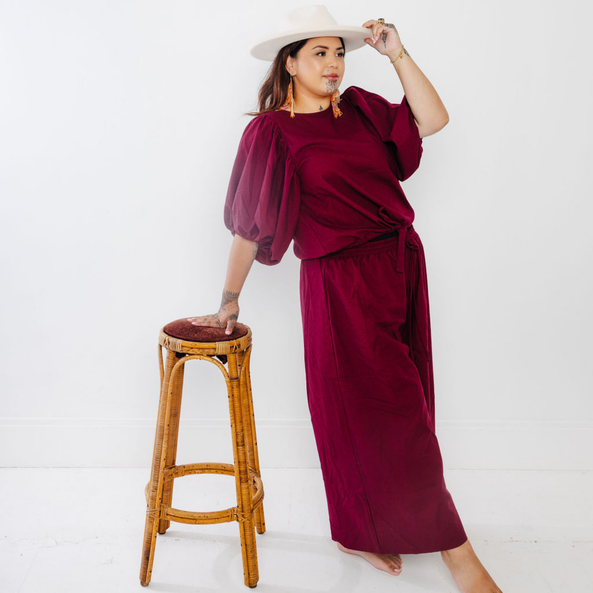 Jonique Oli, founder of waiapu road, wearing the kapua top and wide leg cullotes in plum, leaning against a cane bar stool